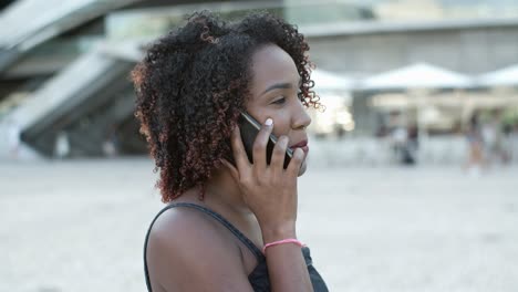 Smiling-curly-woman-talking-with-interlocutor-through-phone
